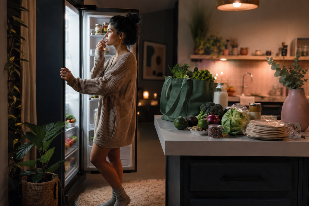 late-night-meat-craving-plant-based-beginner A plant-based beginner looking into the fridge during a late-night craving moment in a cozy kitchen.