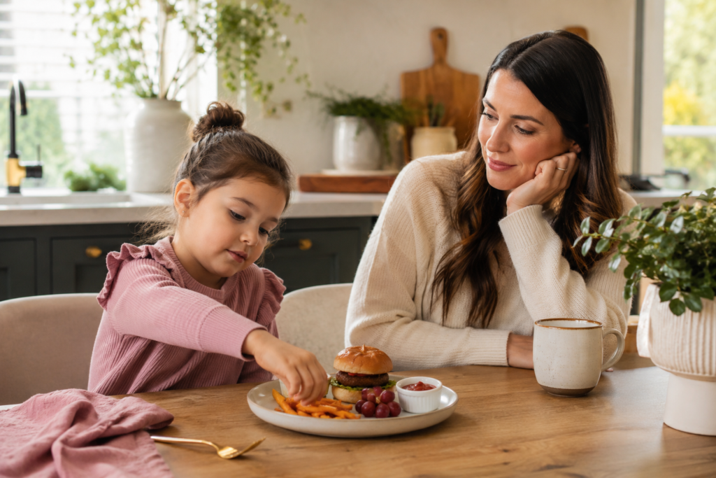 A parent gently introducing plant-based food to a picky eater with a simple plate of a veggie burger slider, fries, grapes, and ketchup.