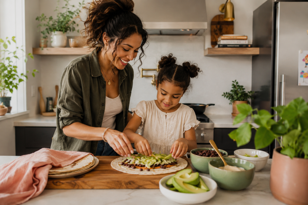  Parent and child making plant-based wraps together with avocado, beans, lettuce, and dairy-free sauce in a cozy kitchen.
